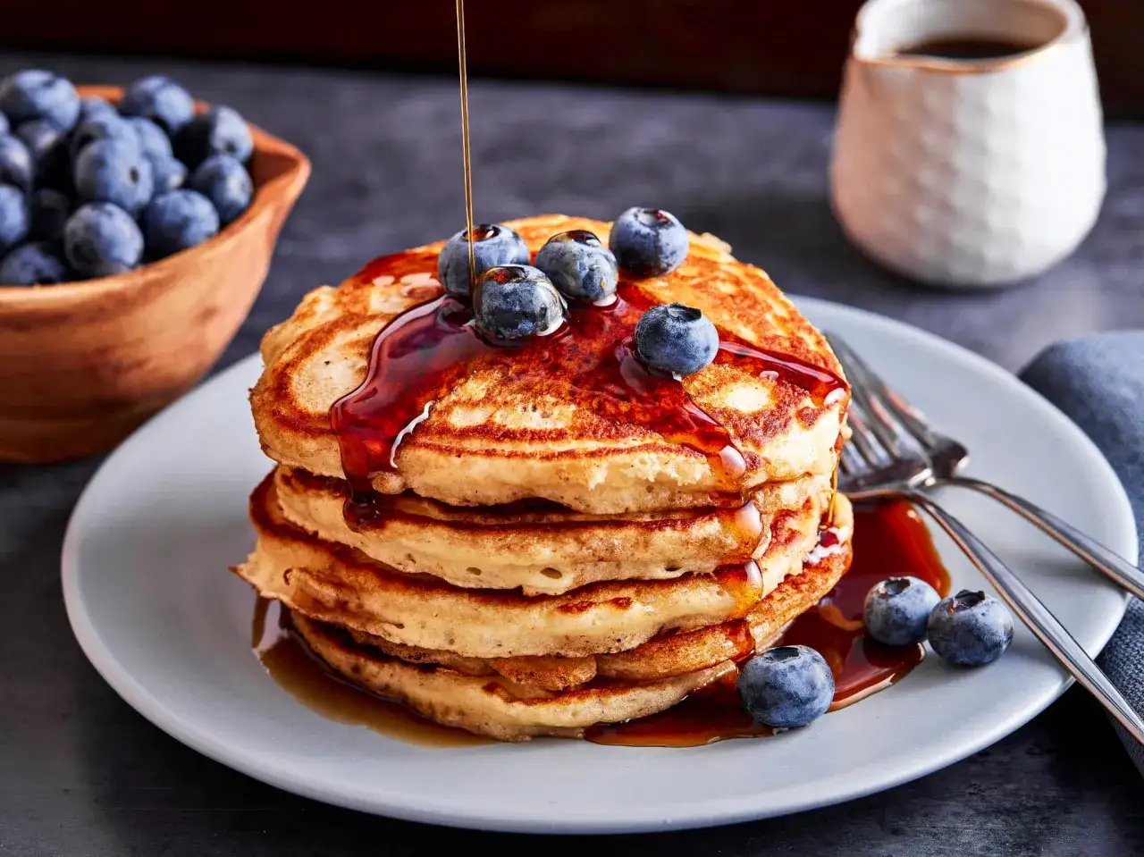 Ein Stapel goldbrauner Pancakes, betr&auml;ufelt mit Sirup und garniert mit Blaubeeren. Ein k&ouml;stliches Pancakes Rezept f&uuml;r den perfekten Brunch.