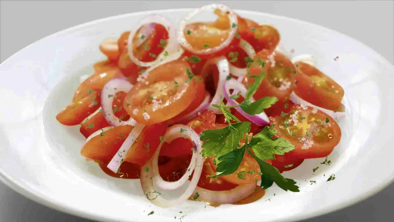 Frischer Tomatensalat mit Zwiebelringen und Petersilie, verfeinert mit einem leichten Dressing.
