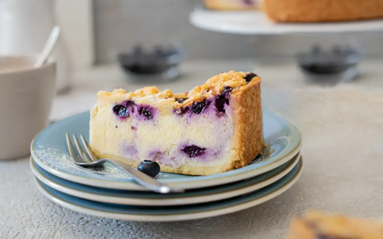 Ein Stück saftiger Blaubeerkuchen mit Streuseln auf einem blauen Teller. Dieses Blaubeerkuchen Rezept ist ein Genuss!