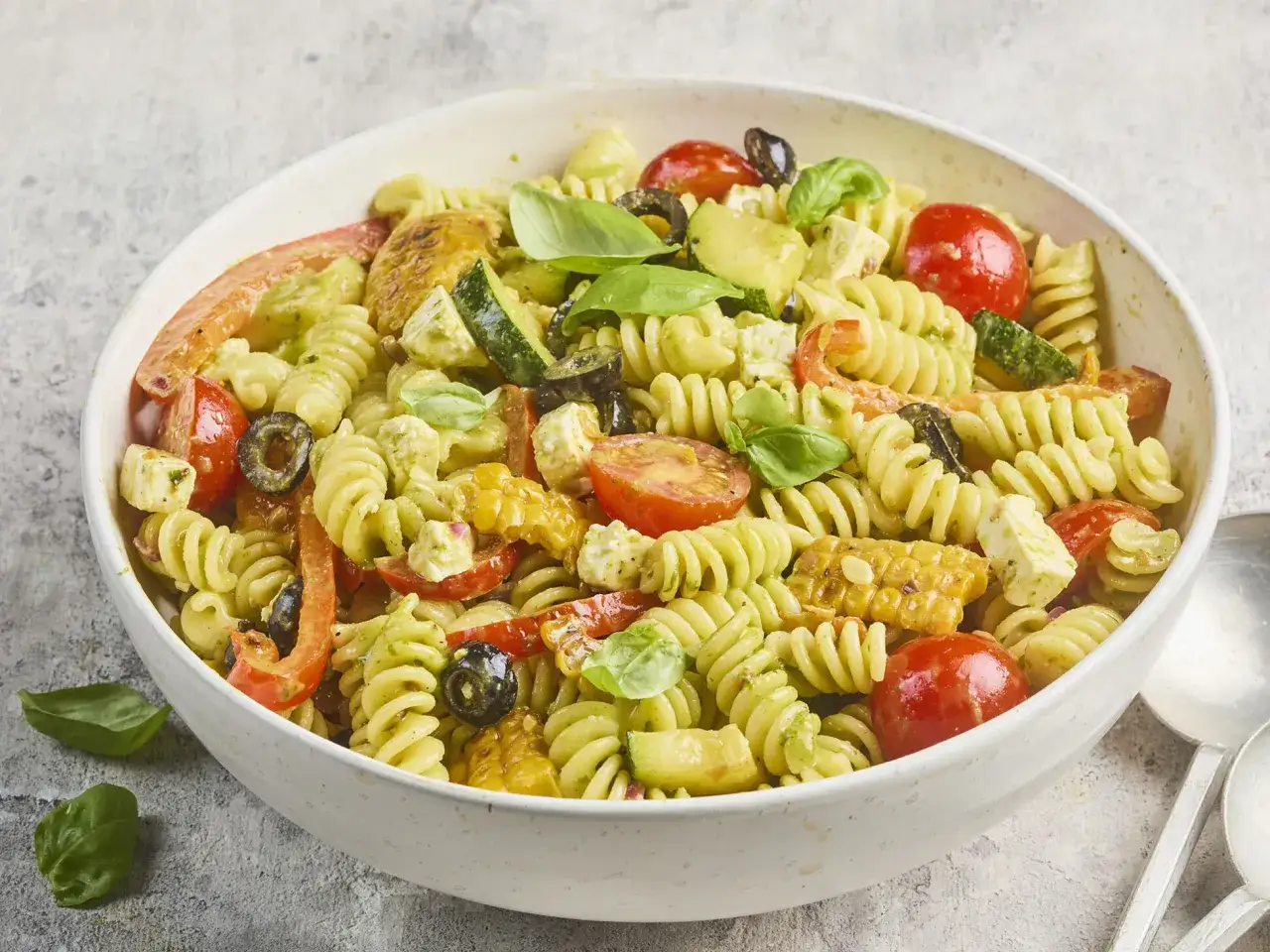 Ein bunter, sommerlicher Nudelsalat mit Fusilli, Kirschtomaten, Zucchini, Oliven, Feta und Maiskolben, verfeinert mit frischem Basilikum.