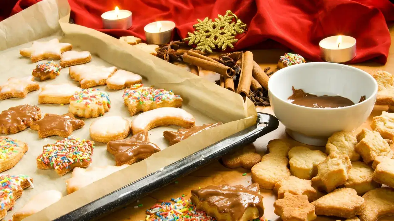Vielfältige weihnachtskekse sorten: Sterne, Herzen und Monde, einige mit Zuckerguss, Schokolade oder bunten Streuseln verziert. Zimtstangen und Kerzen sorgen für festliche Stimmung.