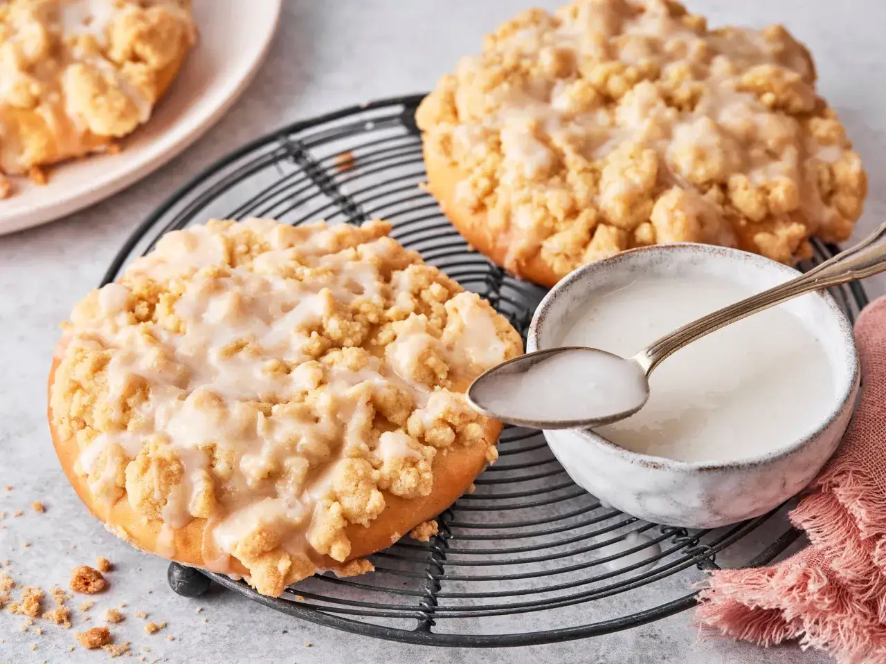 Zwei leckere Streusel Taler mit Zuckerguss auf einem Gitter, daneben eine Schale mit Zuckerguss und ein L&ouml;ffel.