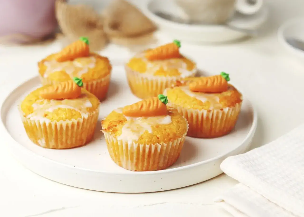 F&uuml;nf leckere Karotten Muffins mit Zuckerguss und Marzipan-Karotten-Deko auf einem Teller.