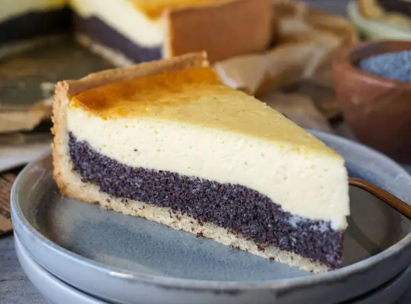 Ein Stück Mohnkuchen mit cremigem Käse-Topping und Mohnback-Schicht auf einem grauen Teller.