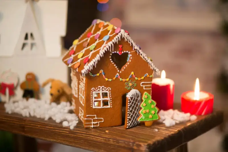 Ein zauberhaftes Lebkuchenhaus, das Lust macht, es selber zu machen. Verziert mit bunten Smarties und Zuckerguss, steht es neben Kerzen und Weihnachtsfiguren.